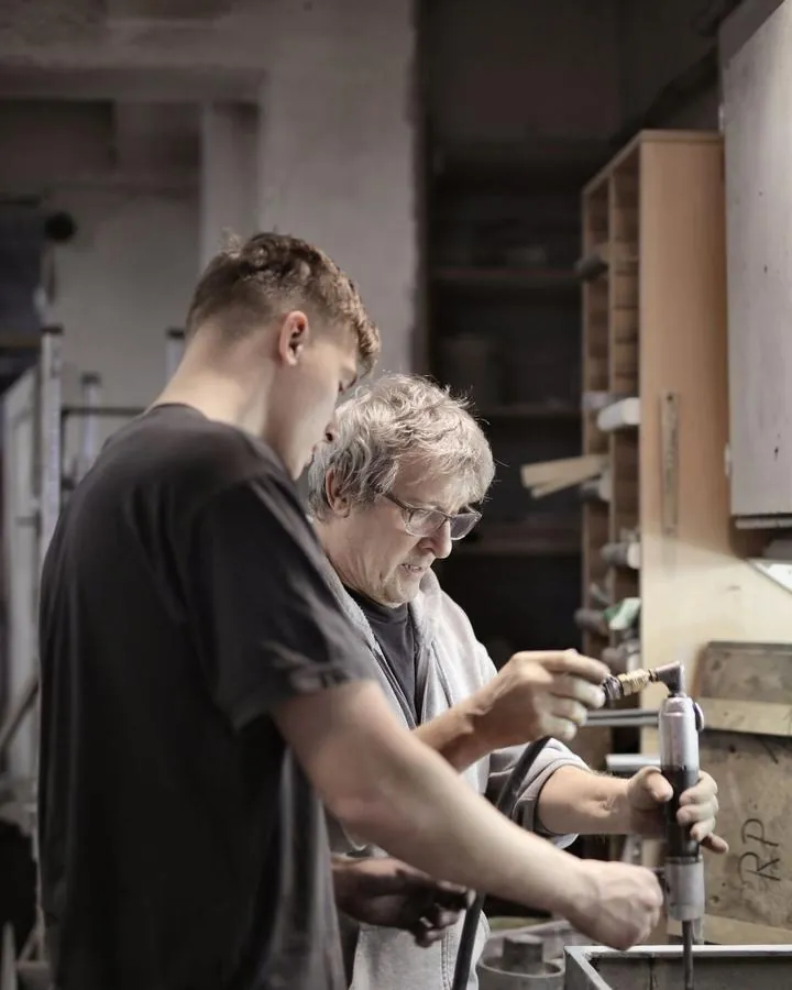 An experienced tradesman showing a young trainee how to use a tool in a workshop