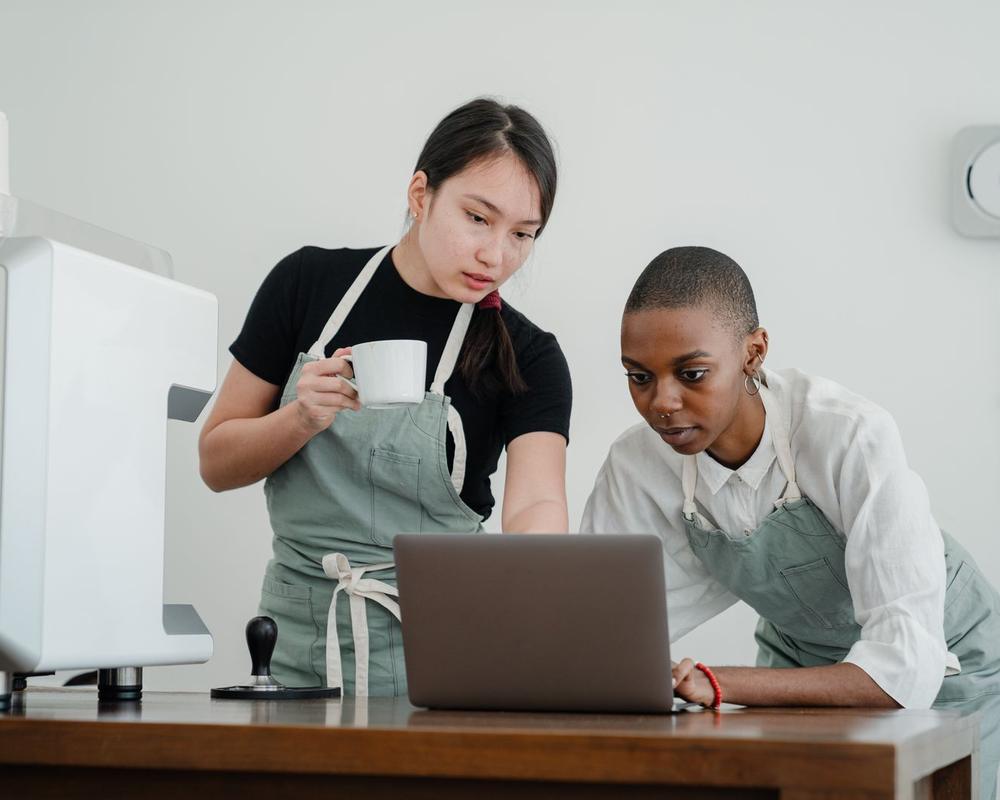 An experienced barista showing a new team member the café system