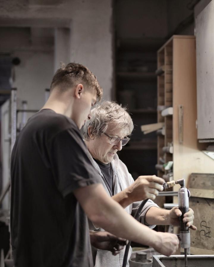 An experienced tradesman showing a young trainee how to use a tool in a workshop